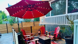 Eine Terrasse mit roten Adirondack-Stühlen, einem kleinen Tisch und einem roten Sonnenschirm.