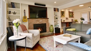 Ein Wohnzimmer mit Kamin, Gitarre, Bücherregal und einer Couch.