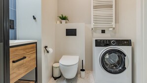 Une salle de bain moderne avec des toilettes, un lave-linge et une petite plante accrochée au mur.