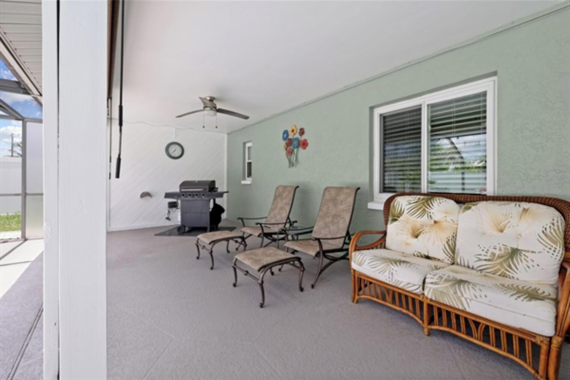A covered patio area with a ceiling fan, a grill, two chairs, and a sofa.