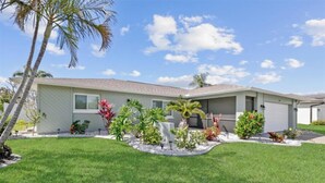 Una casa de planta baixa amb teulada plana, un garatge i un jardí ben cuidat amb diverses plantes i una palmera.