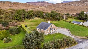 A house with a sloped roof, surrounded by well-maintained lawns and hedges, set in a rural landscape with hills in the background. - Teach Eile, on the outskirts of Clifden (Clifden)