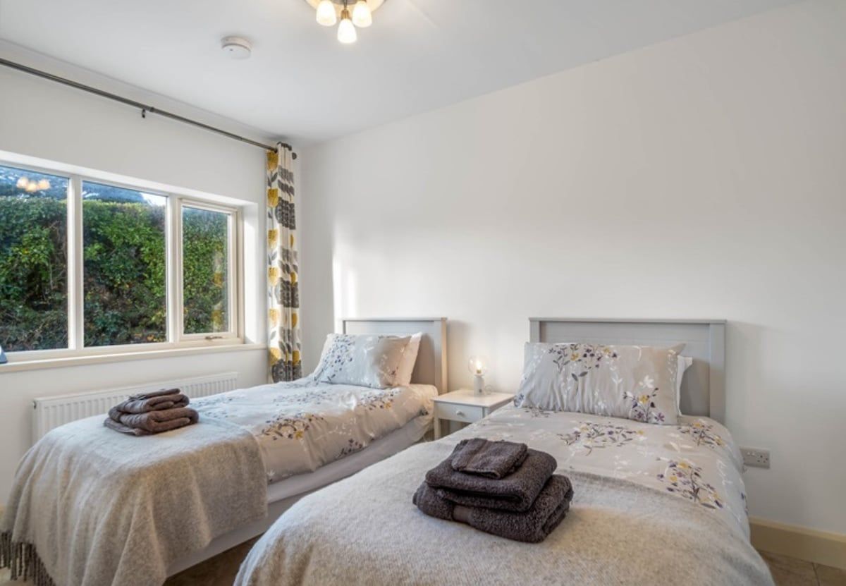 A bedroom with two beds, a window with curtains, and a radiator.
