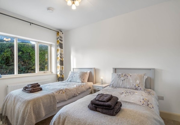 A bedroom with two beds, a window with curtains, and a radiator.