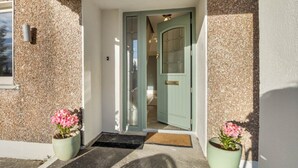 A building entrance with a stone facade, a green door, and two potted plants with pink flowers. - Teach Eile, on the outskirts of Clifden (Clifden)