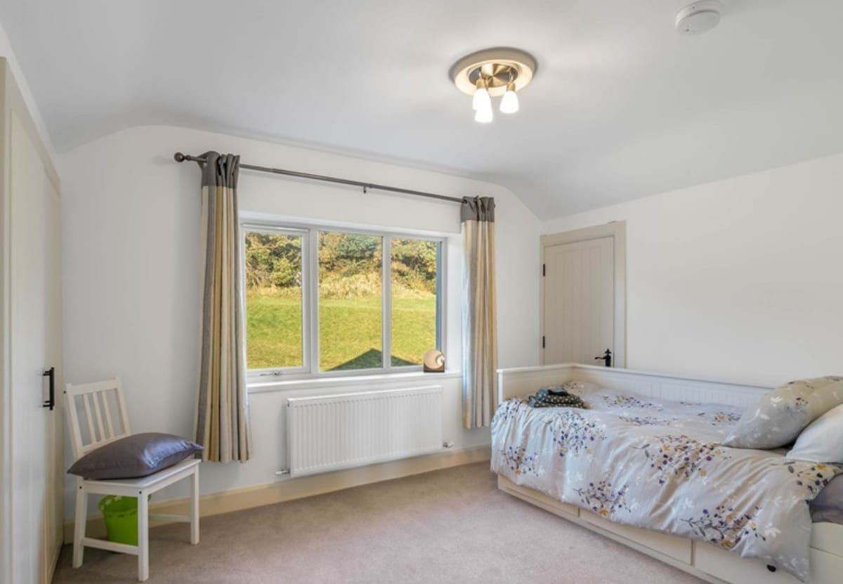 A bedroom with a bed, a chair, a window with curtains, a radiator, and a door.