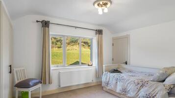 Une chambre à coucher avec un lit, une chaise, une fenêtre avec des rideaux, un radiateur et une porte.