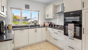 A modern kitchen with white cabinets, a black oven, and a window with a view of a house and trees. - Teach Eile, on the outskirts of Clifden (Clifden)