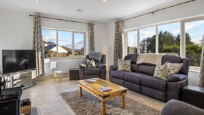A modern living room with a sofa, armchair, and coffee table. There is a flat-screen TV and a radiator. - Teach Eile, on the outskirts of Clifden (Clifden)