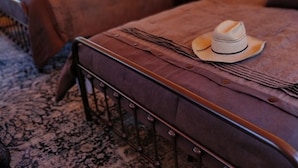 Une chambre confortable, aménagée comme une tente, avec deux lits, un chapeau et une lanterne posés sur une table de chevet.
