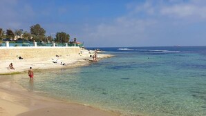 A beach with clear shallow waters, a sandy shore, and a few people relaxing. - Peaceful Haven With Stunning Views Close to sea (Marsaskala)