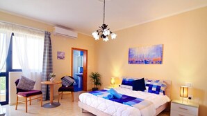 A bedroom with a bed, bedside tables, a chair, a small table, a painting, and an air conditioning unit. - Peaceful Haven With Stunning Views Close to sea (Marsaskala)