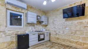 A compact kitchen with stone walls, a built-in oven, a small refrigerator, and a flat-screen TV mounted on the wall.