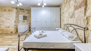 A bedroom with a stone wall, a bed with white linens, a wardrobe, and a bedside table.