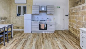 A compact kitchen with a refrigerator, stove, and sink, wooden flooring, and a small dining area with chairs. - Lovely 1BR Studio home in Quiet Town of Zejtun (Iż-Żejtun)