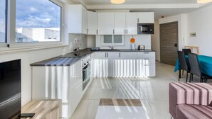 A modern kitchen with white cabinets, a black countertop, and a dining area with a teal tablecloth. - Sunny 2BR Penthouse with Spacious Rooftop Terrace (San Ġwann)
