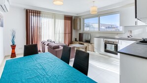 A modern living room with a sofa, a dining table, and a kitchen area with a TV and cabinets. - Sunny 2BR Penthouse with Spacious Rooftop Terrace (San Ġwann)