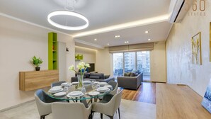 A modern living room with a glass dining table, grey sofas, and a city view. - Luxury 3BR home in St Julians with private terrace (St. Julian`s)