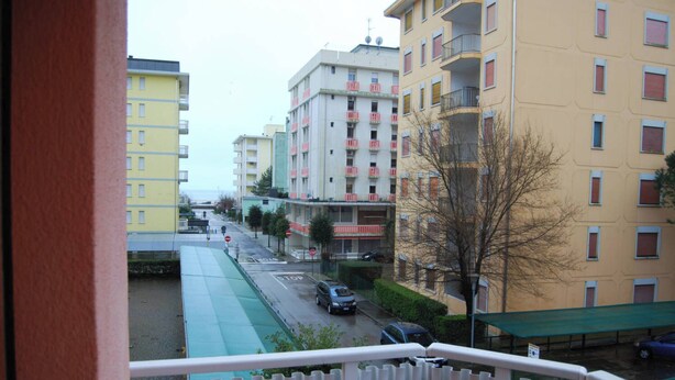A view from a balcony overlooking a street with multi-story buildings, a green bike lane, and parked cars.