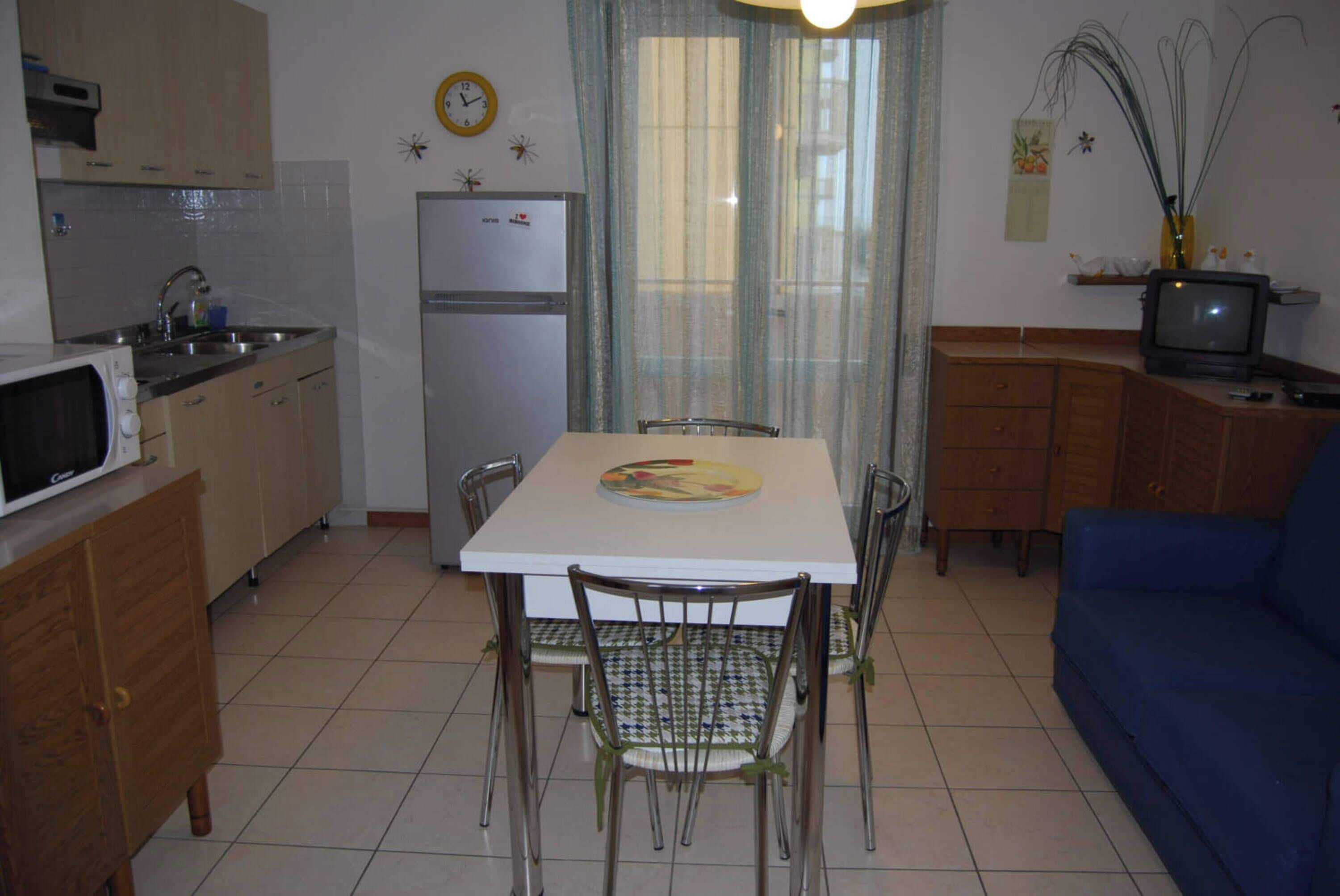 A compact kitchen with a dining table, chairs, a microwave, a refrigerator, and a blue sofa.