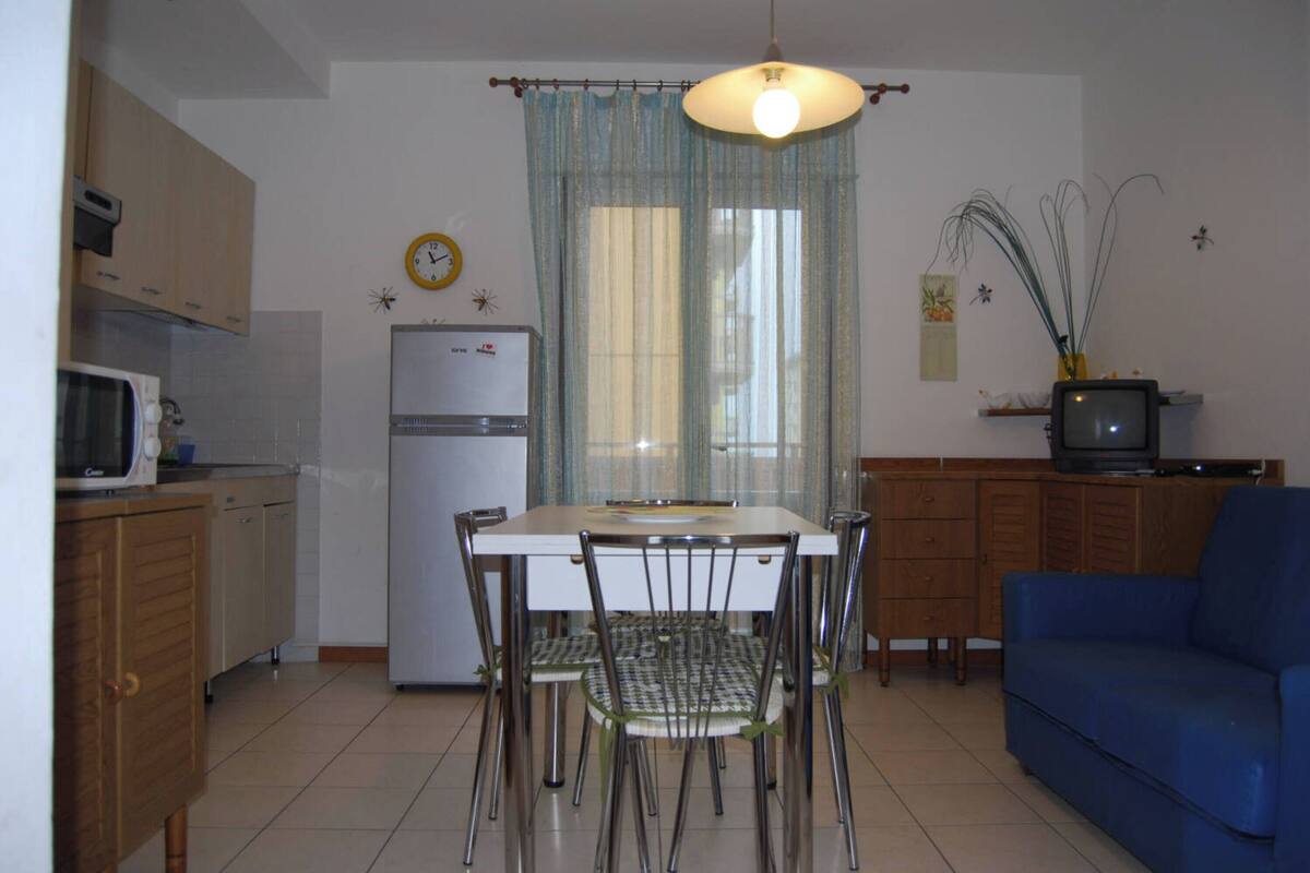 A compact kitchen with a dining table, chairs, a refrigerator, a microwave, and a television.