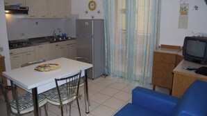 A compact kitchen with a refrigerator, stove, and sink. There is a dining table with chairs and a blue sofa in the living area.