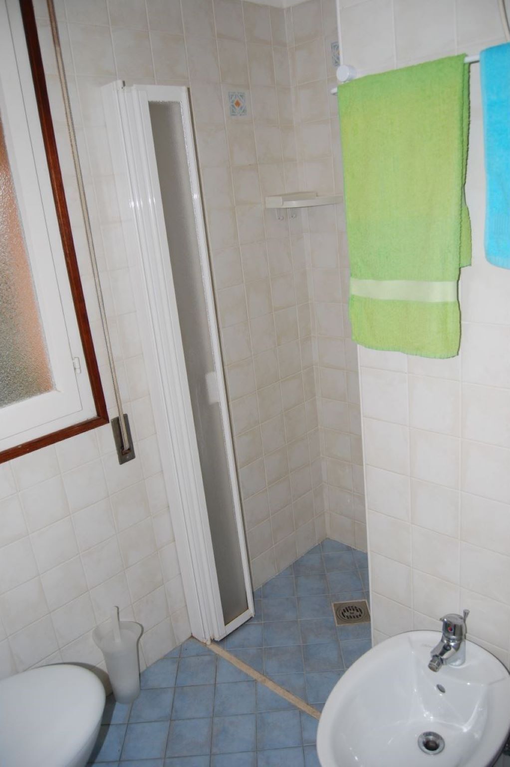 Un bagno con un lavandino bianco, un water, una doccia con porta in vetro e un asciugamano verde appeso al muro.