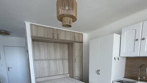 Pieni huone, jossa on sänky, pieni keittiönurkkaus ja vaatekaappi.