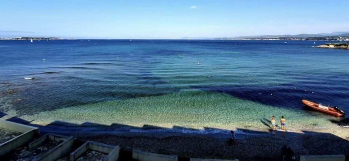 En strand med klart vatten, en båt och människor på stranden.