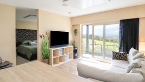A modern living room with a flat-screen TV, a sofa, a dining table, and a large window offering a view of the countryside. - Core-na-bye (Inverness)
