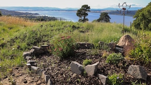 A garden with a stone wall, a metal sculpture, and a sign indicating a cabin. - Core-na-bye (Inverness)