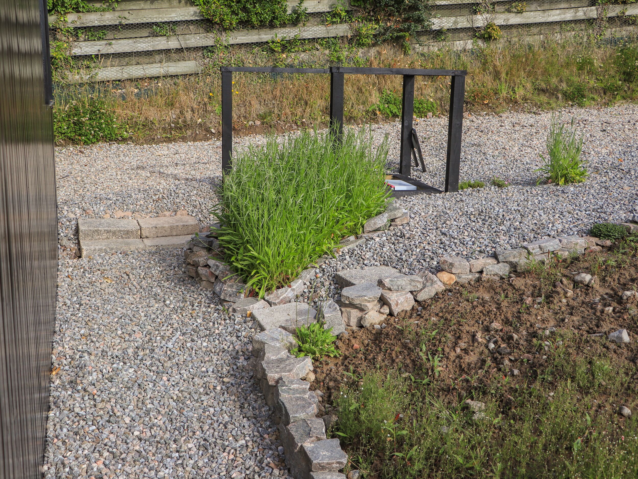 Ein Garten mit einem Kiesweg, einem Holzzaun und einem Metalltor.