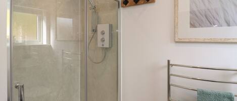 A modern bathroom with a glass-enclosed shower, a towel rack with green towels, and a framed artwork on the wall.