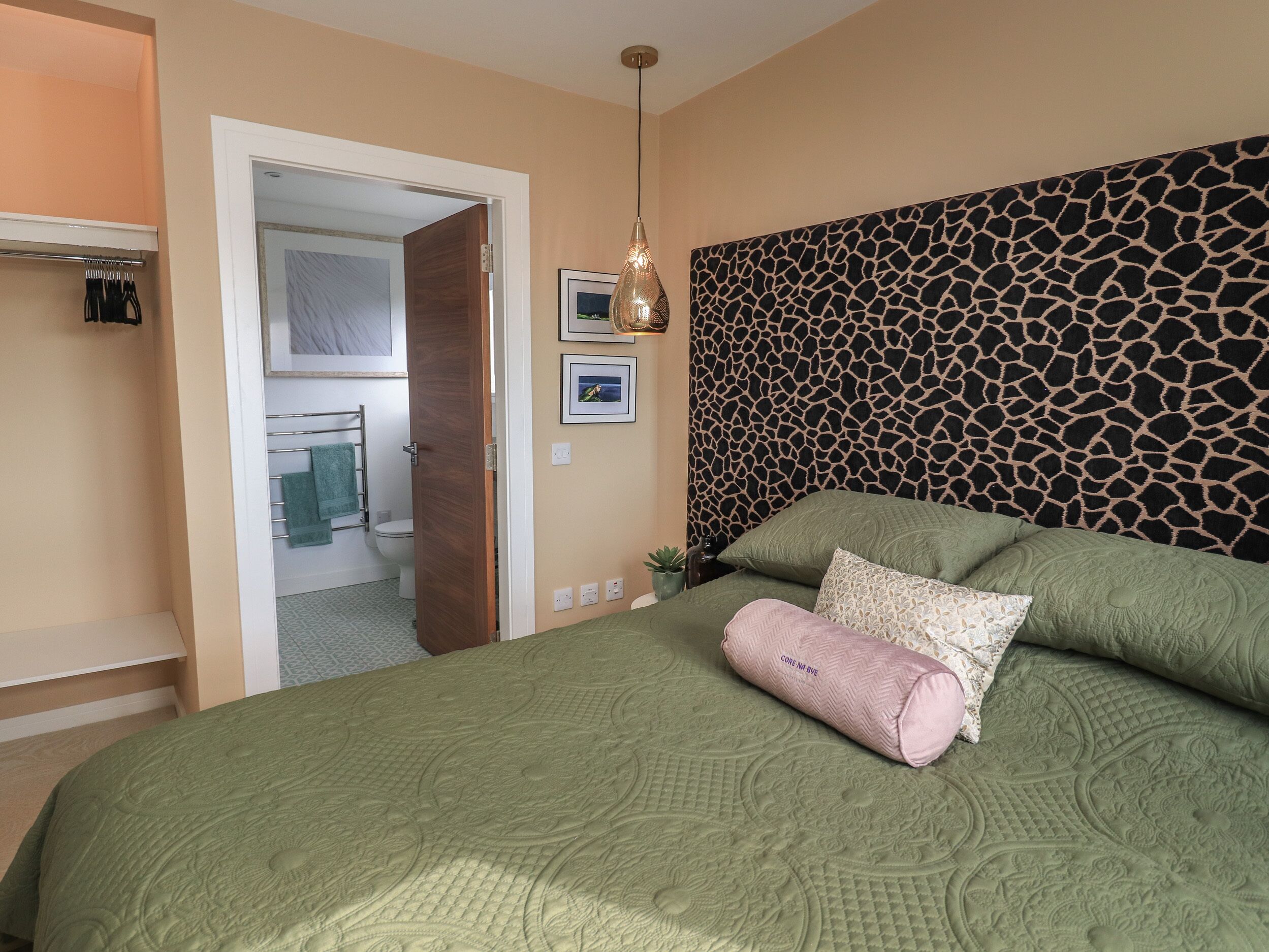 Un dormitorio con una cama verde, cabecera con estampado de jirafa y una lámpara colgante.