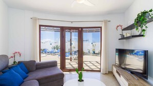Ein modernes Wohnzimmer mit einer Couch, einem Couchtisch, einem Fernseher und einem Balkon mit Blick auf einen Pool.