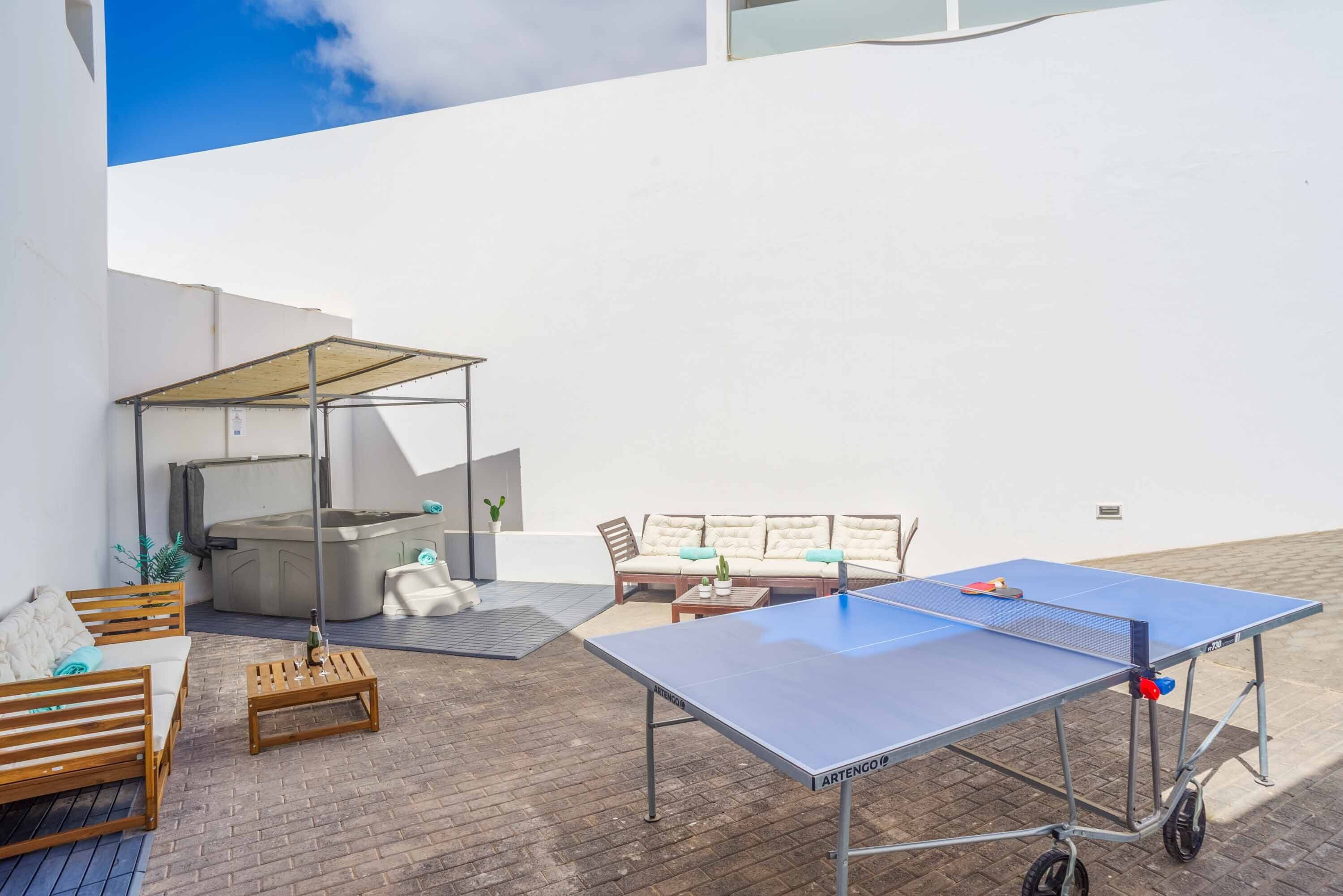 Une table de ping-pong, un canapé, une petite table avec une bouteille et un jacuzzi dans un espace patio extérieur.