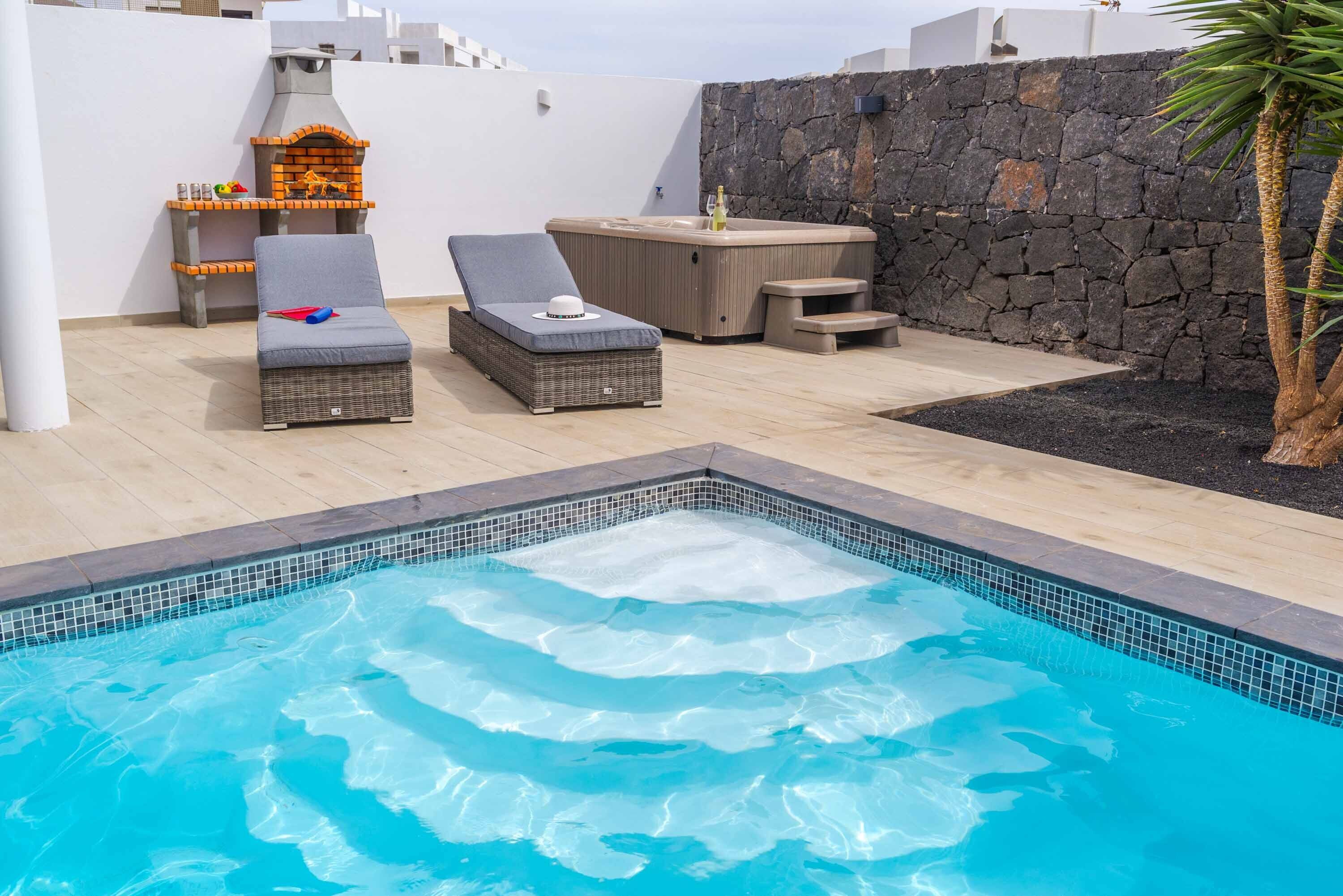 A swimming pool with lounge chairs and a hot tub.