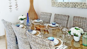 A dining area with wicker chairs, a glass table, and white flowers.