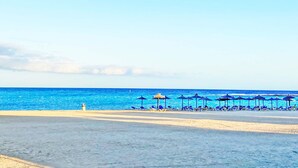 A beach with blue umbrellas and lounge chairs.