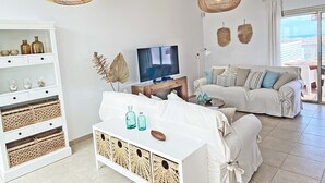 A modern living room with a white sofa, a television, wicker baskets, and a view of the city through the window.