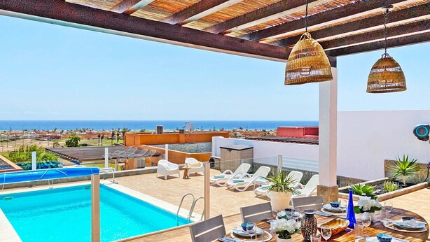 A rooftop pool area with a dining table set for four, overlooking a coastal landscape.