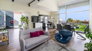 Una sala moderna con sofá, comedor con sillas, cocina y un amplio ventanal con vistas.