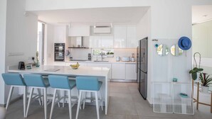 Una cocina moderna con armarios blancos, una isla central con taburetes de bar y un refrigerador empotrado.
