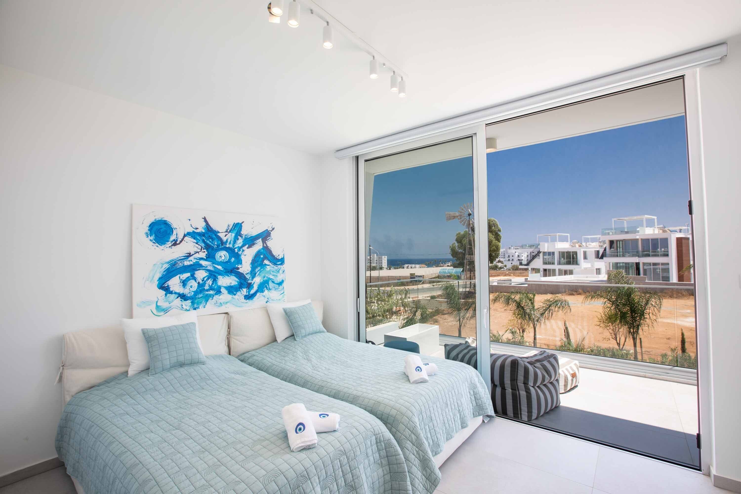 Une chambre moderne avec deux lits, une grande fenêtre et une vue sur des immeubles et des palmiers.