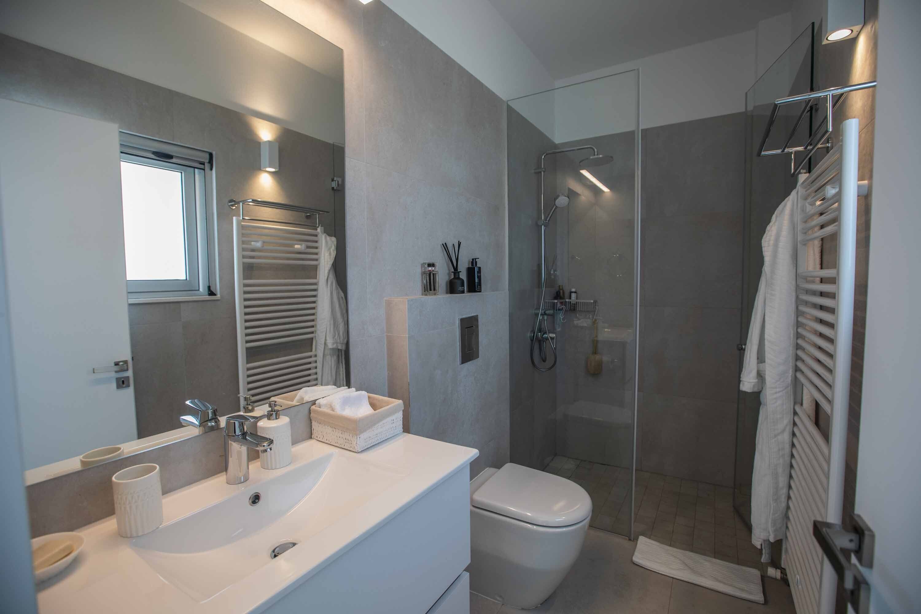 A modern bathroom with a large mirror, a white sink, a toilet, and a glass-enclosed shower area.