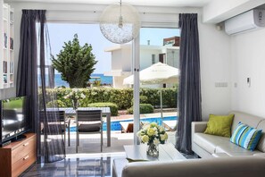 Un salon moderne avec un téléviseur, un canapé et une vue sur une piscine et l’océan.