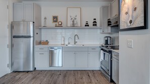 A modern kitchen with white cabinets, stainless steel appliances, and a wooden floor.