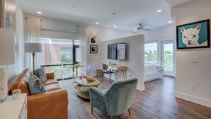 A modern living room with a leather sofa, a grey armchair, a wooden coffee table, and a flat-screen TV mounted on the wall.