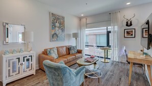 A modern living room with a sofa, armchair, and a dining table. There is a cabinet with glass doors and a mounted deer head.