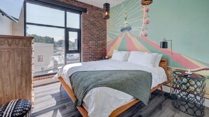 A modern hotel room with a large bed, a view of the city, and a colorful mural on the wall. - The Hive 205 Sweeter (Wilmington)